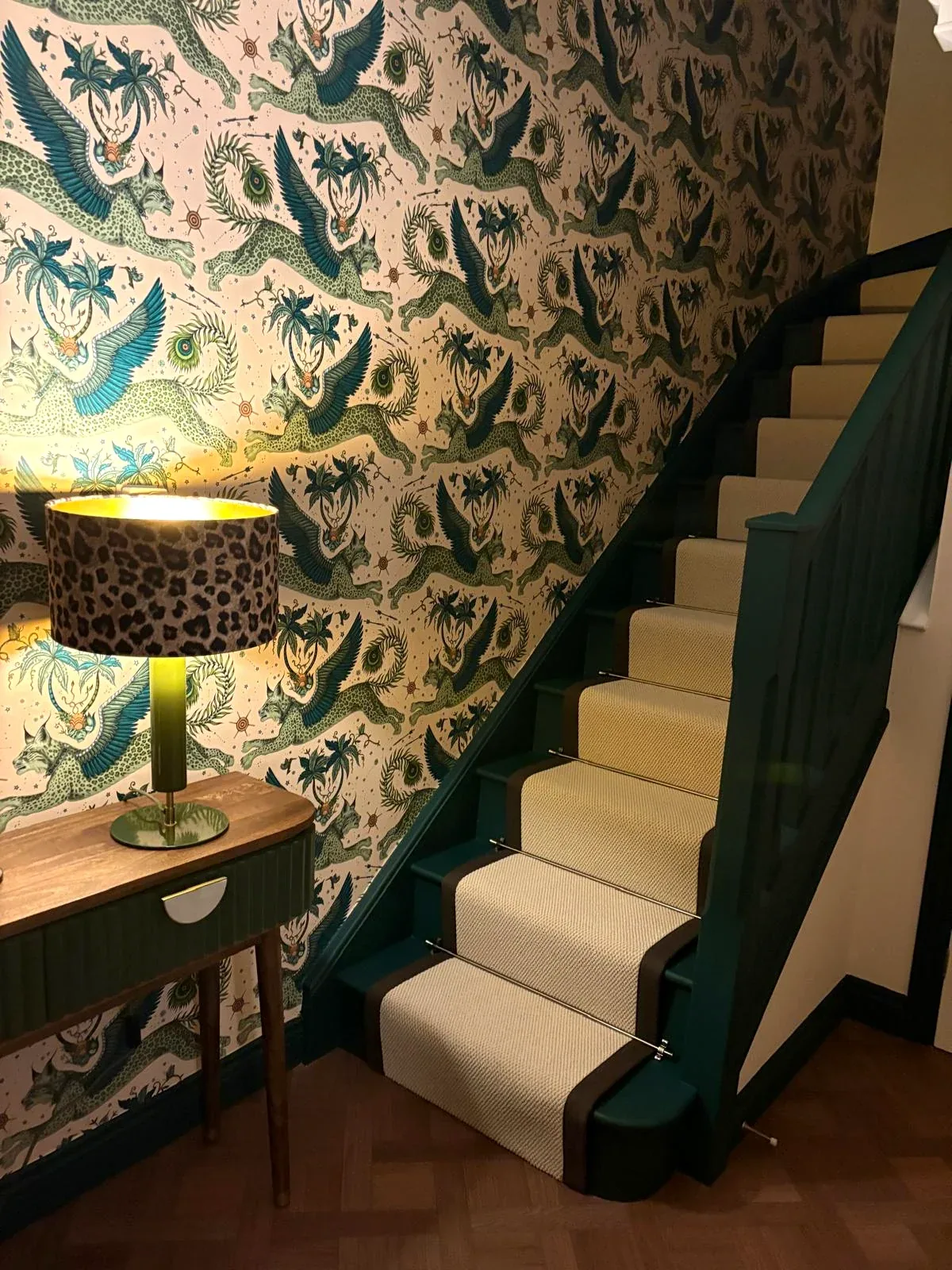 Finished staircase with patterned wallpaper, dark green woodwork and cream stair runner