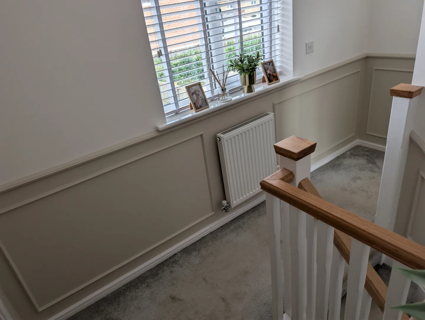 Pale painted wall panelling beside a wooden handrail on a landing